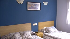 A bedroom with two beds, patterned bedding, a nightstand, and a framed picture on the wall. - Pensión Gema Irun (Irun)
