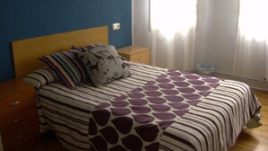 A bedroom with a bed, nightstands, a window with curtains, and a wall-mounted light fixture. - Pensión Gema Irun (Irun)