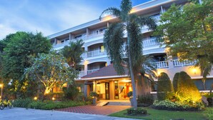 Een meerlaags hotel met een centrale ingang, omgeven door weelderige begroeiing en palmbomen.