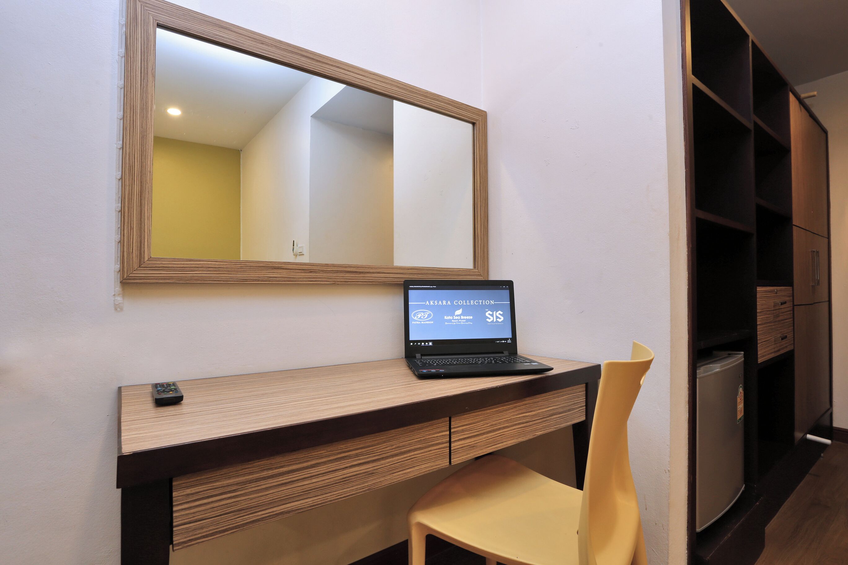 Un espacio de trabajo moderno con una computadora portátil, un espejo, una silla y un refrigerador.
