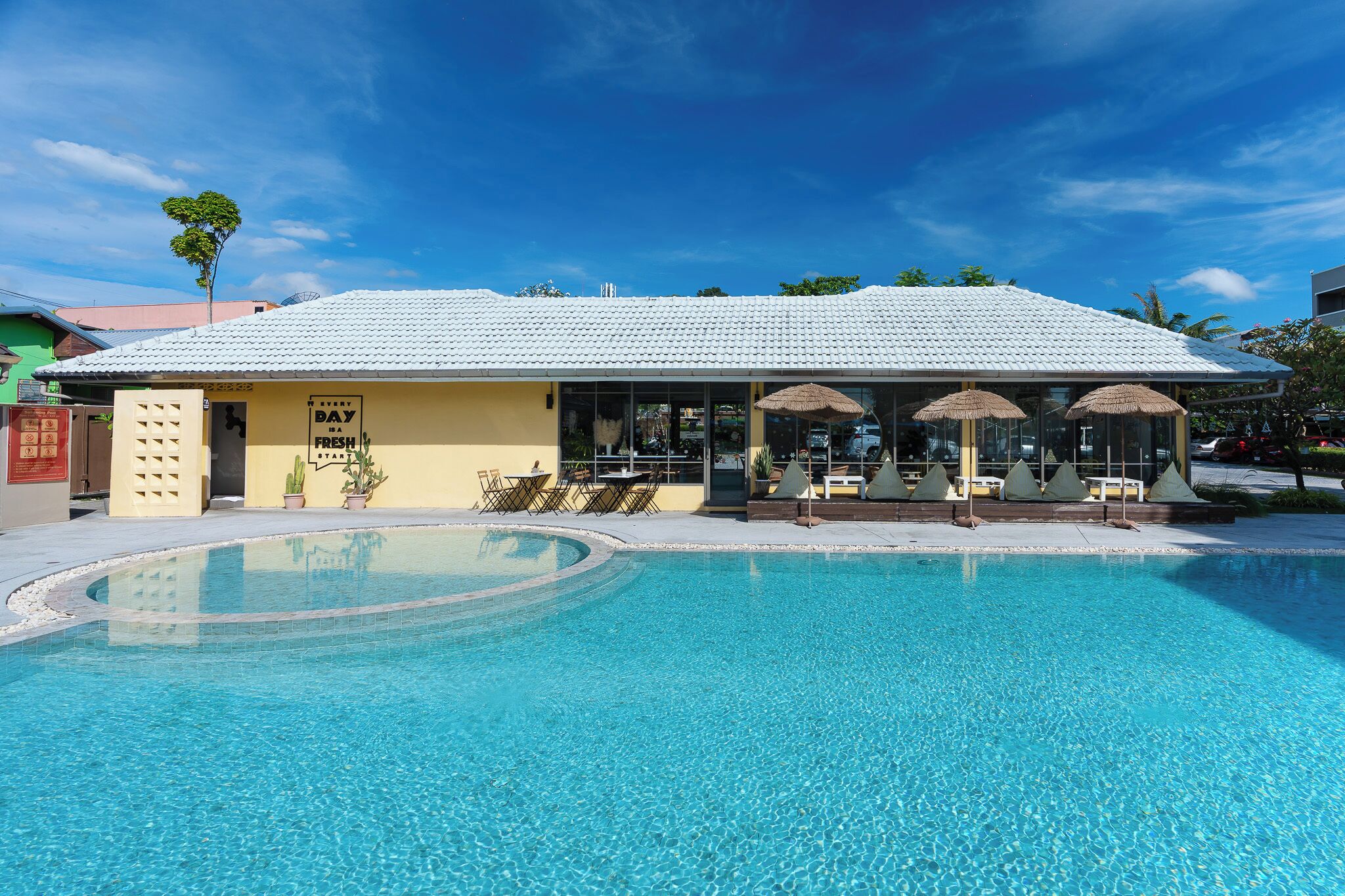 A poolside area with a building featuring a tiled roof, outdoor seating, and a clear blue pool.