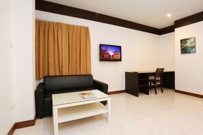 A living room with a black leather sofa, a glass coffee table, a TV on the wall, and a desk with a chair. - Pattra Mansion by AKSARA Collection (Phuket)