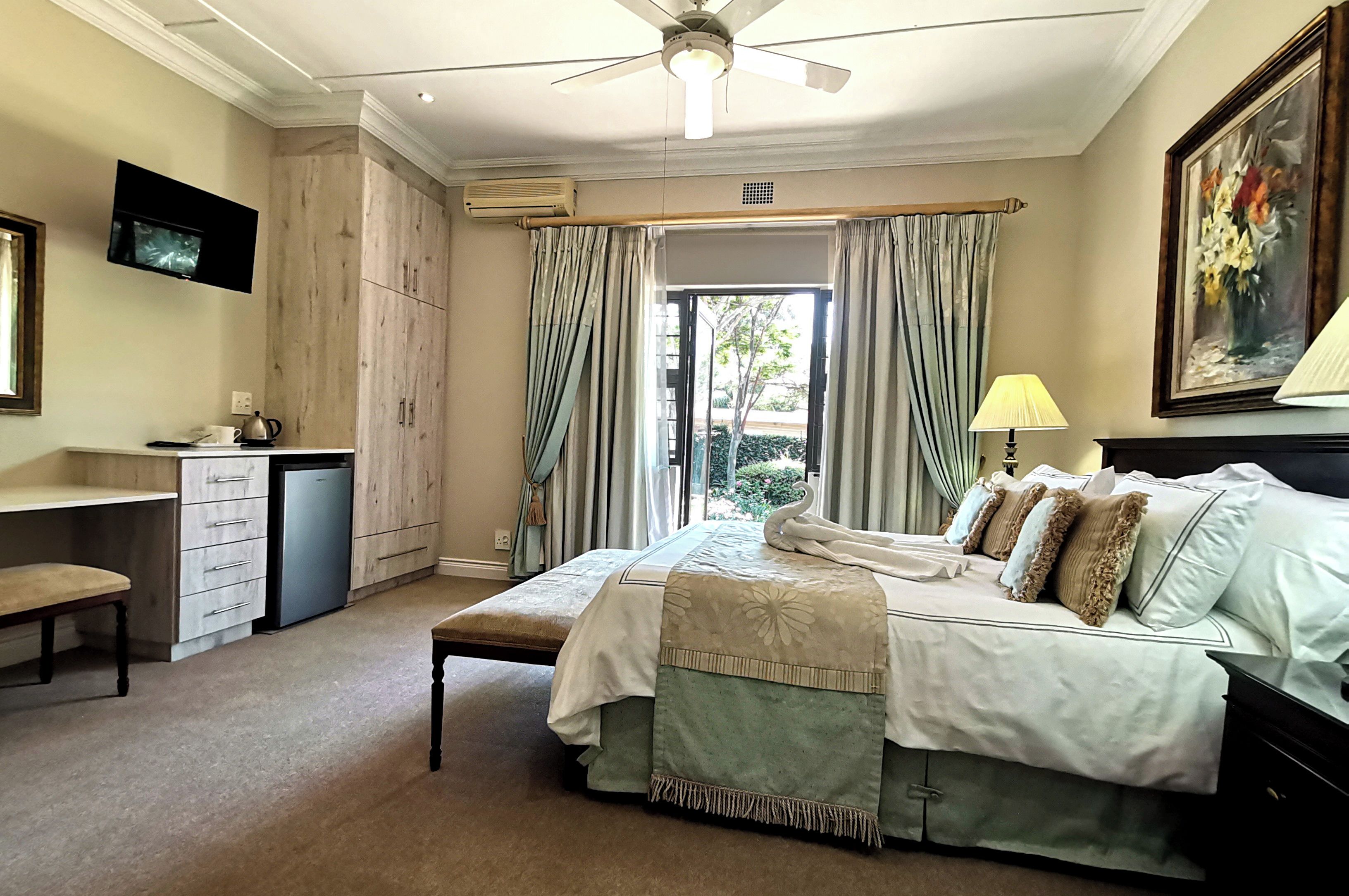 A bedroom with a bed, bedside table, desk, chair, and a television mounted on the wall.