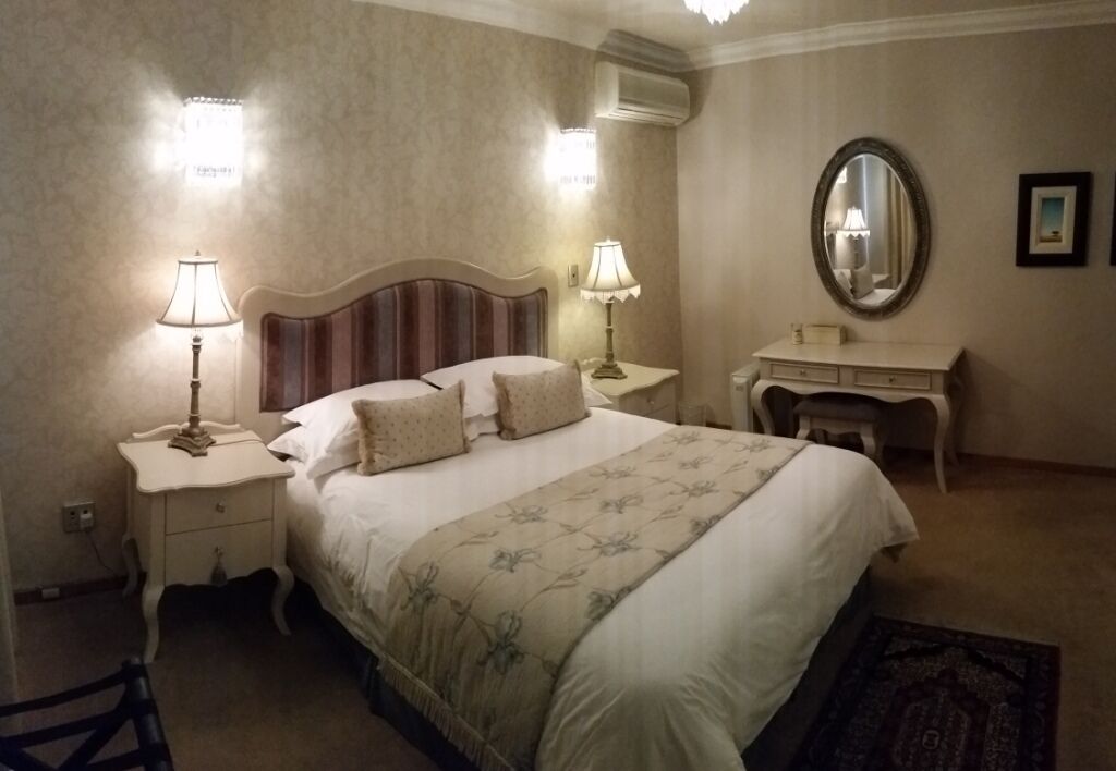 A hotel room with a large bed, two bedside tables with lamps, a dresser, and a mirror.