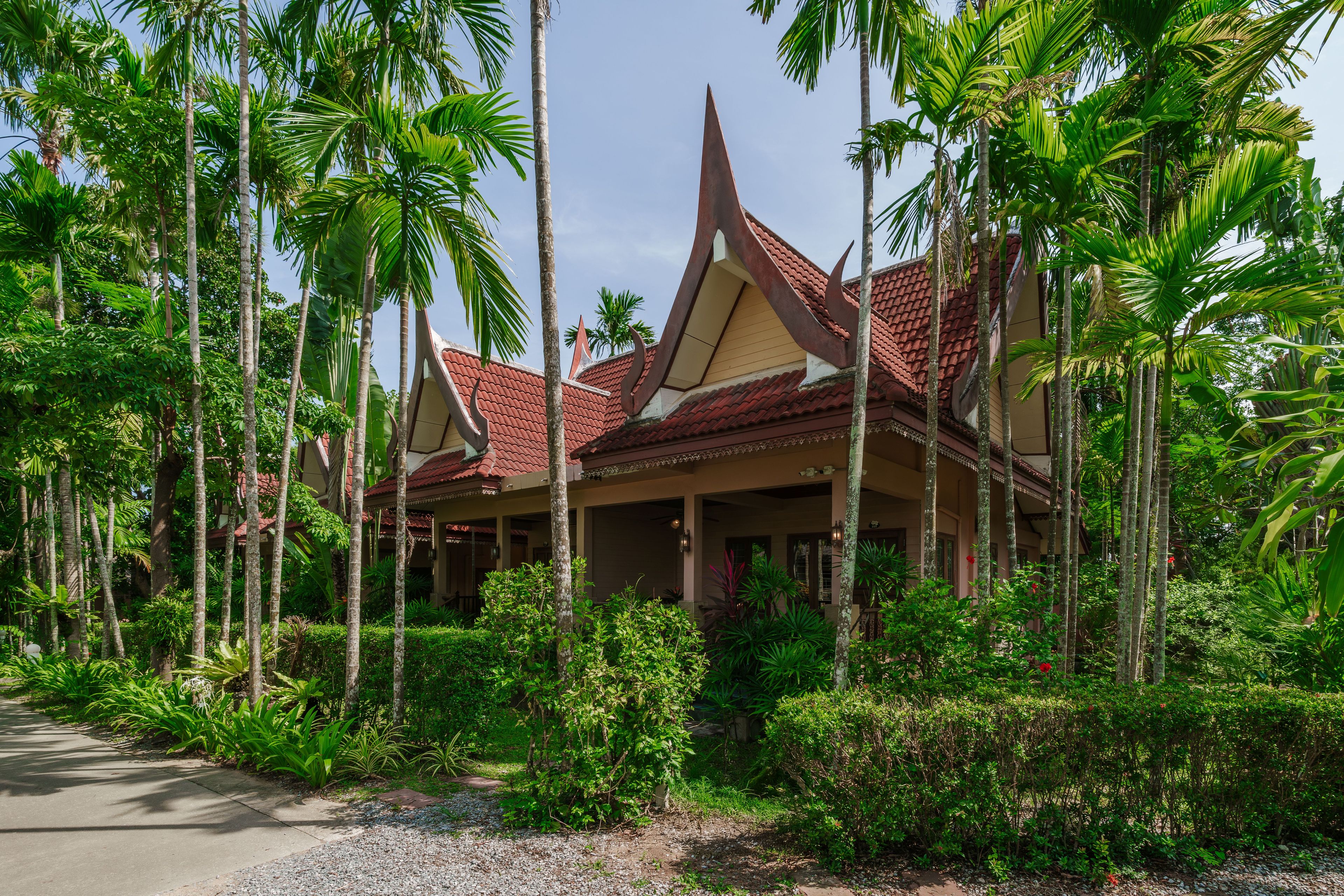 A traditional building with a red tiled roof, surrounded by lush greenery and tall palm trees.