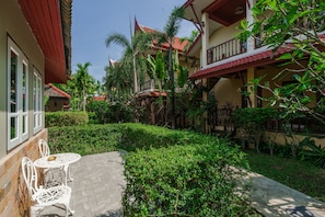 A courtyard with a paved walkway, white metal chairs, and lush greenery. - Palm Village (Rawai)