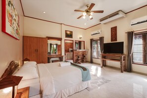 A spacious bedroom with a large bed, a TV, a ceiling fan, and a kitchen area visible through an open door. - Palm Village (Rawai)