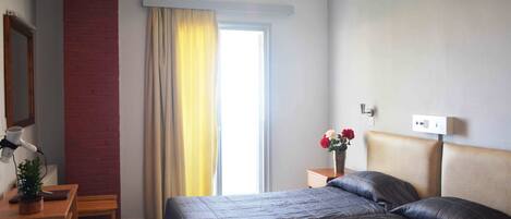 Habitación de hotel con dos camas, una ventana con cortinas, una mesita de noche con lámpara y una planta pequeña.