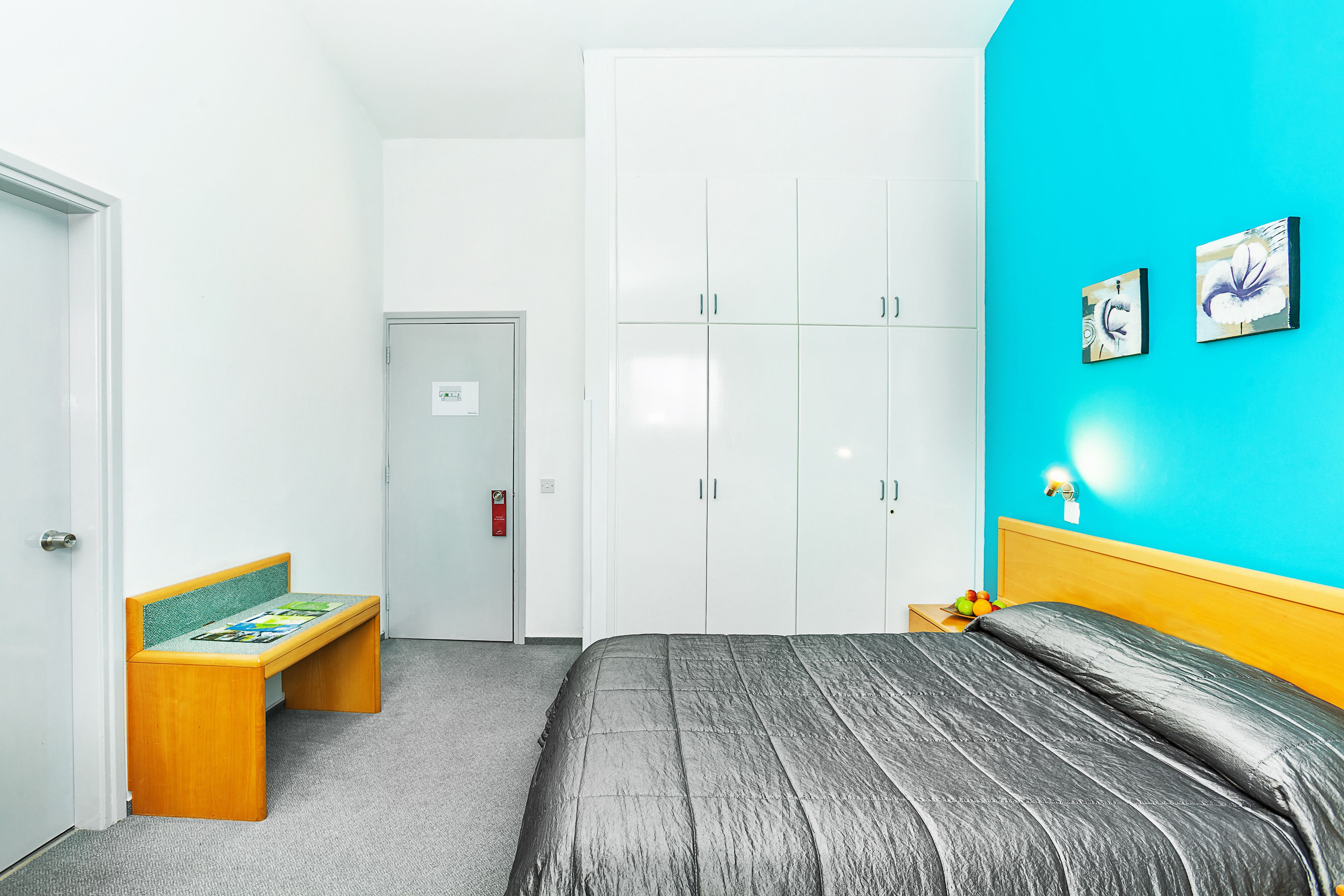 A bedroom with a bed, a bench, a wardrobe, and a wall with two framed pictures.