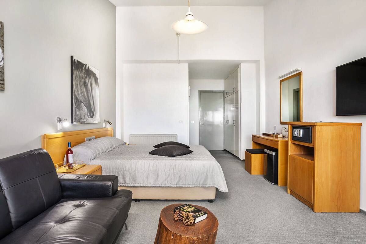 Moderni hotellihuone, jossa on sänky, sohva, työpöytä ja televisio.