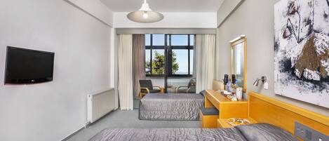 Ein Hotelzimmer mit Bett, Schreibtisch, Stuhl, Fernseher, einem Fenster mit Vorhängen und einem Bild an der Wand.