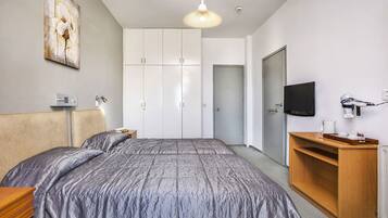 Une chambre à coucher comprenant un lit, une armoire, un téléviseur et un bureau avec une lampe.