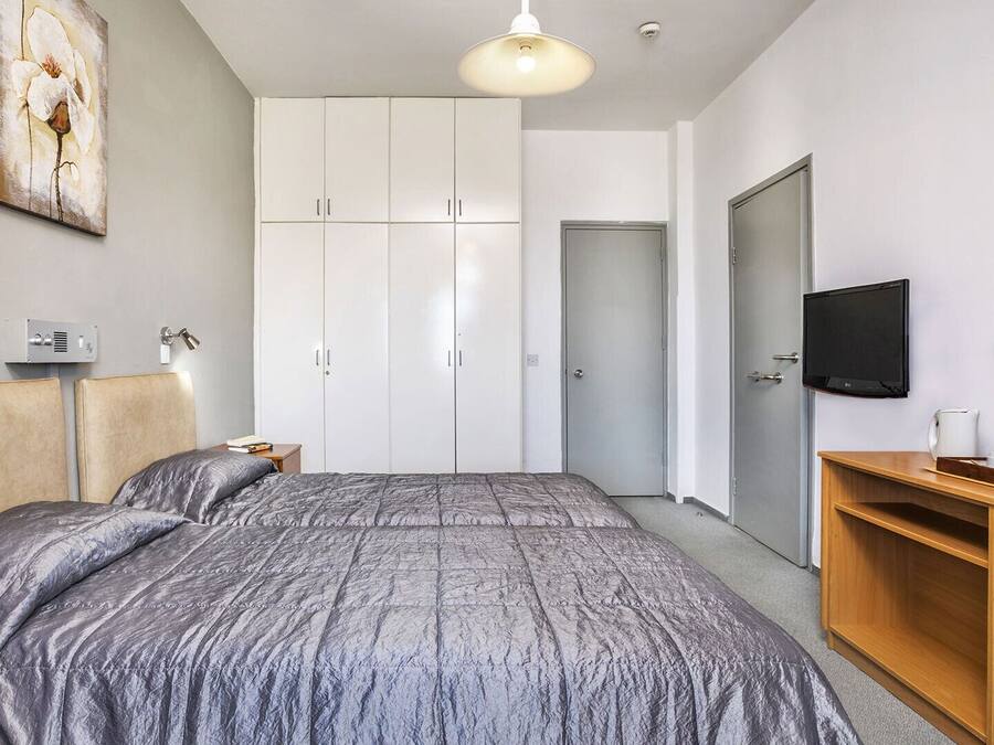 Une chambre à coucher comprenant un lit, une armoire, un téléviseur et un bureau avec une lampe.