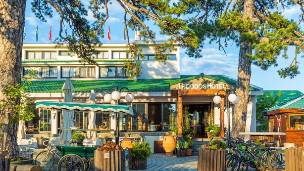 A hotel with a green roof, outdoor seating, and bicycles parked outside. - Troodos Hotel (Troodos)