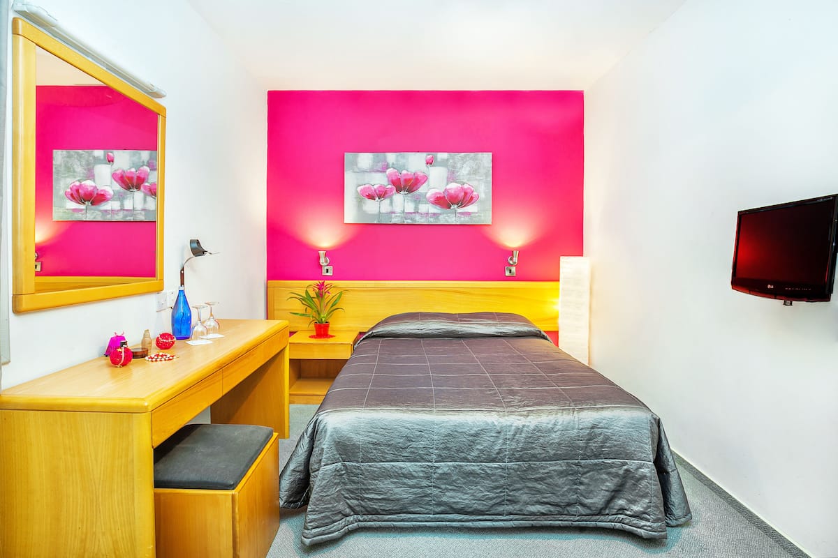 Hotellihuone, jossa on sänky, yöpöytä, lamppu ja seinälle asennettu televisio.