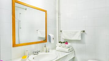 Un baño con un espejo grande, un lavabo, un perchero con toallas y un inodoro.