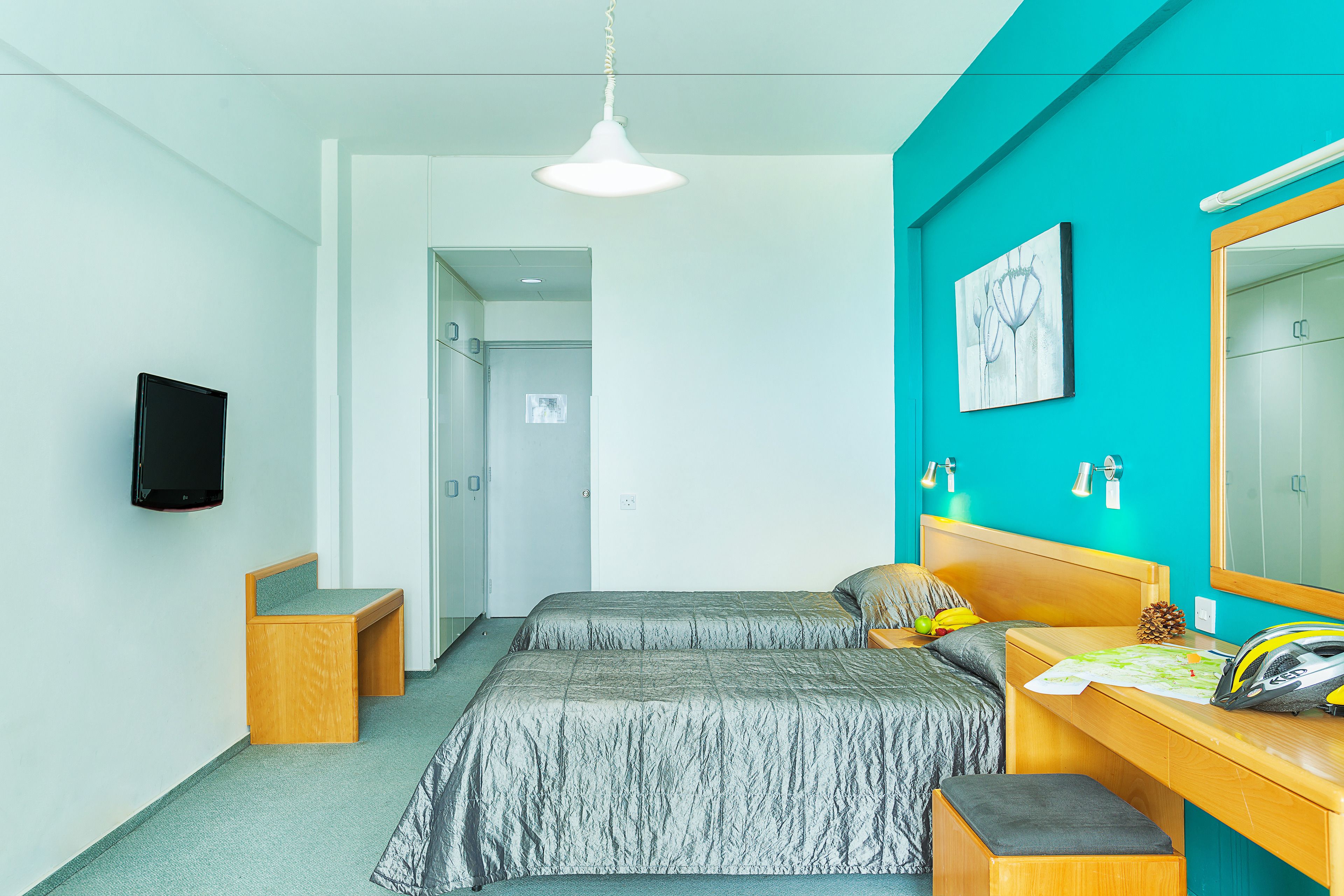 A bedroom with two beds, a desk, a mirror, and a TV.