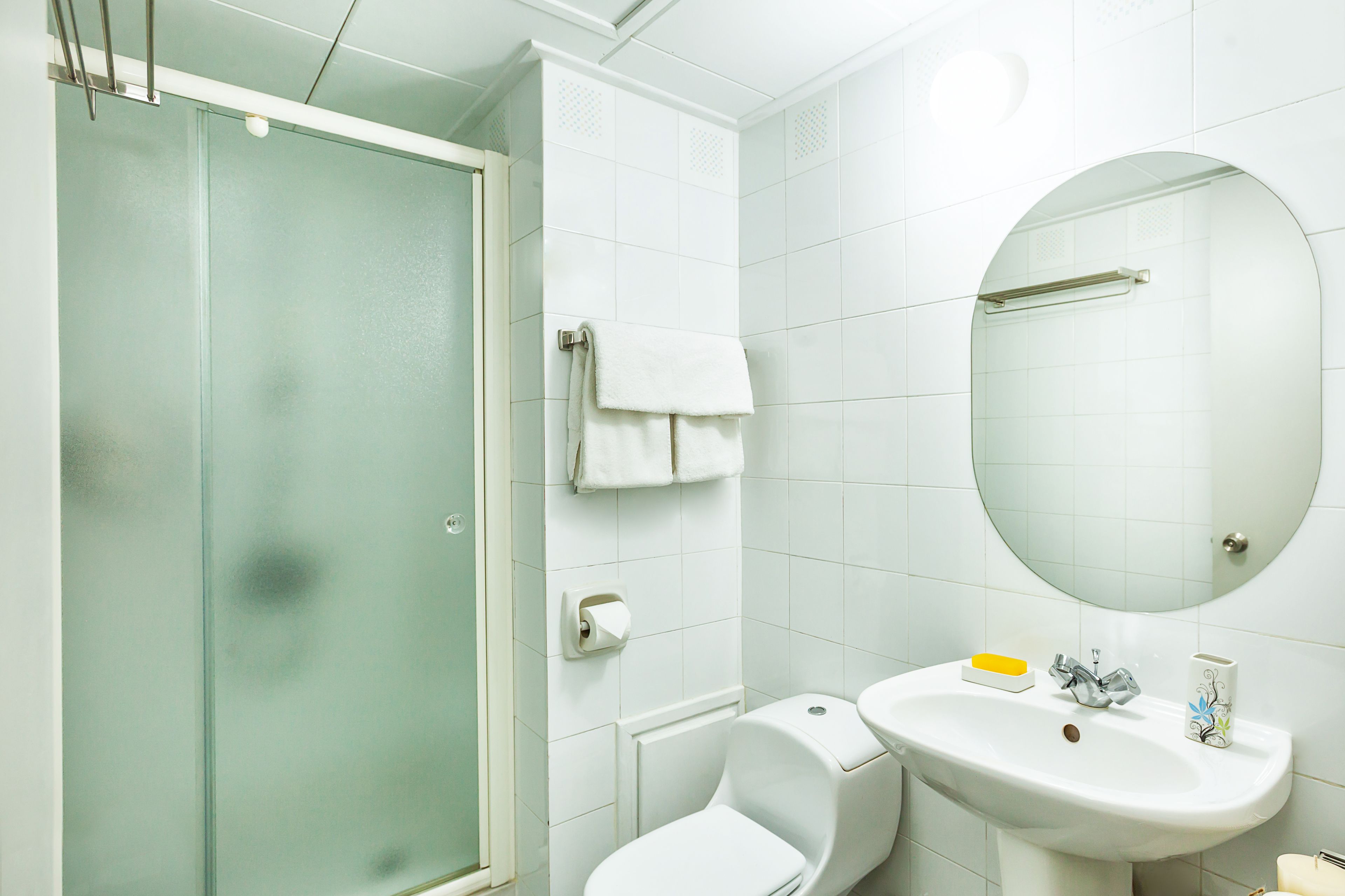 A bathroom with a glass shower enclosure, a white toilet, a sink with a mirror above it, and a towel hanging on the wall.