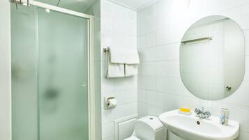 A bathroom with a glass shower enclosure, a white toilet, a sink with a mirror above it, and a towel hanging on the wall.
