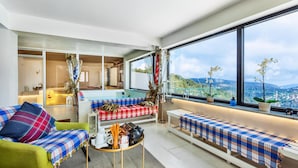 A modern living room with a large window, a sofa, a bench, and a table with a view of the city. - Troodos Hotel (Troodos)