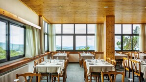 A dining area with tables set for a meal, large windows with curtains, and a view of the outdoors. - Troodos Hotel (Troodos)