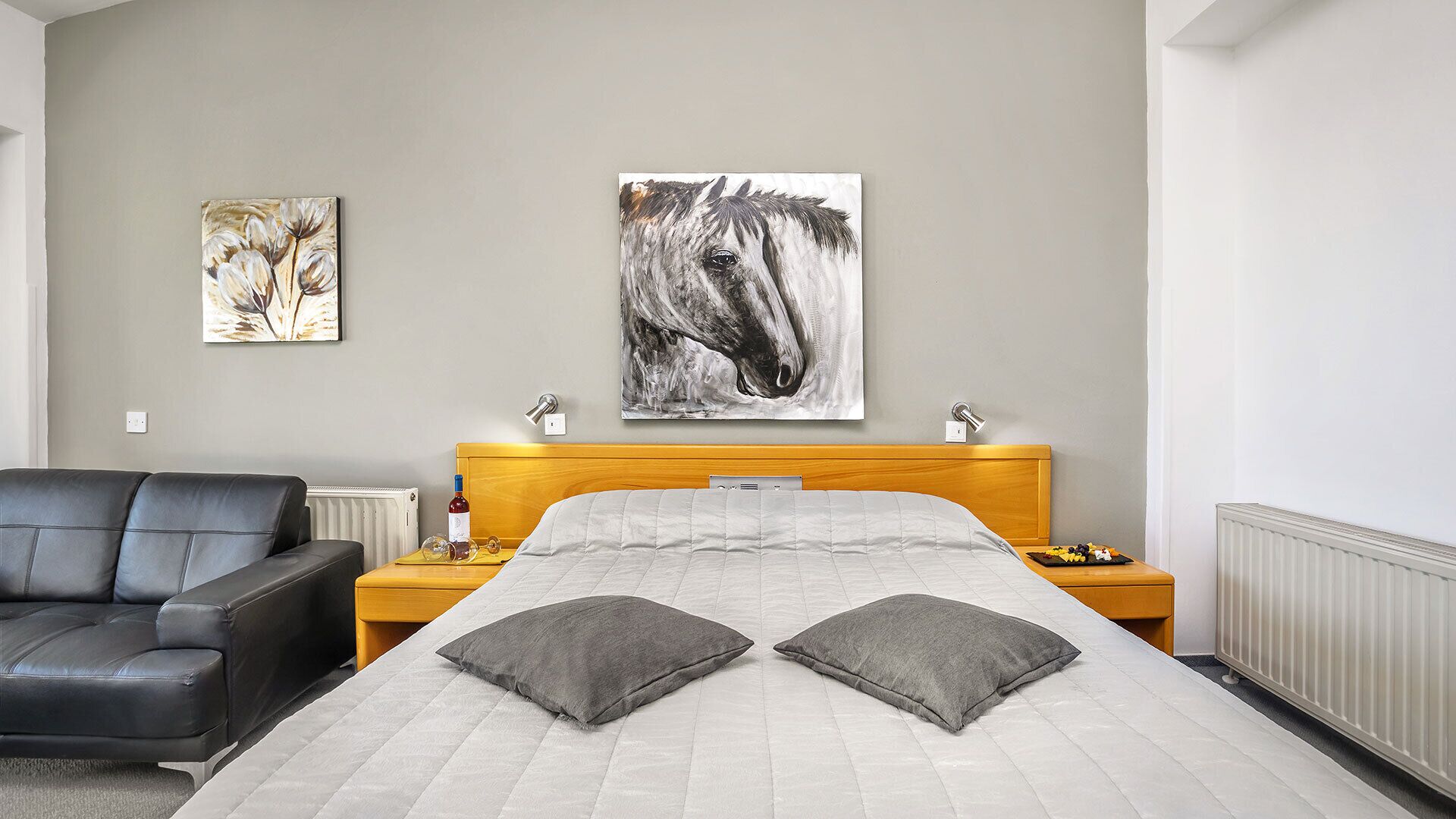 A hotel room with a bed, a nightstand, a chair, and two wall art pieces.