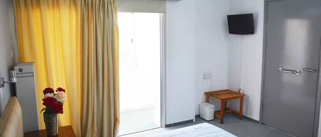 A hotel room with a bed, a small table with a vase of flowers, a television mounted on the wall, and a door.