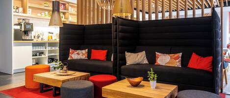 A modern lounge area with a black sofa, wooden coffee table, and orange ottoman.