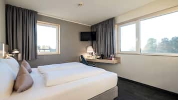 A hotel room with a bed, a desk, a chair, a TV, and large windows.