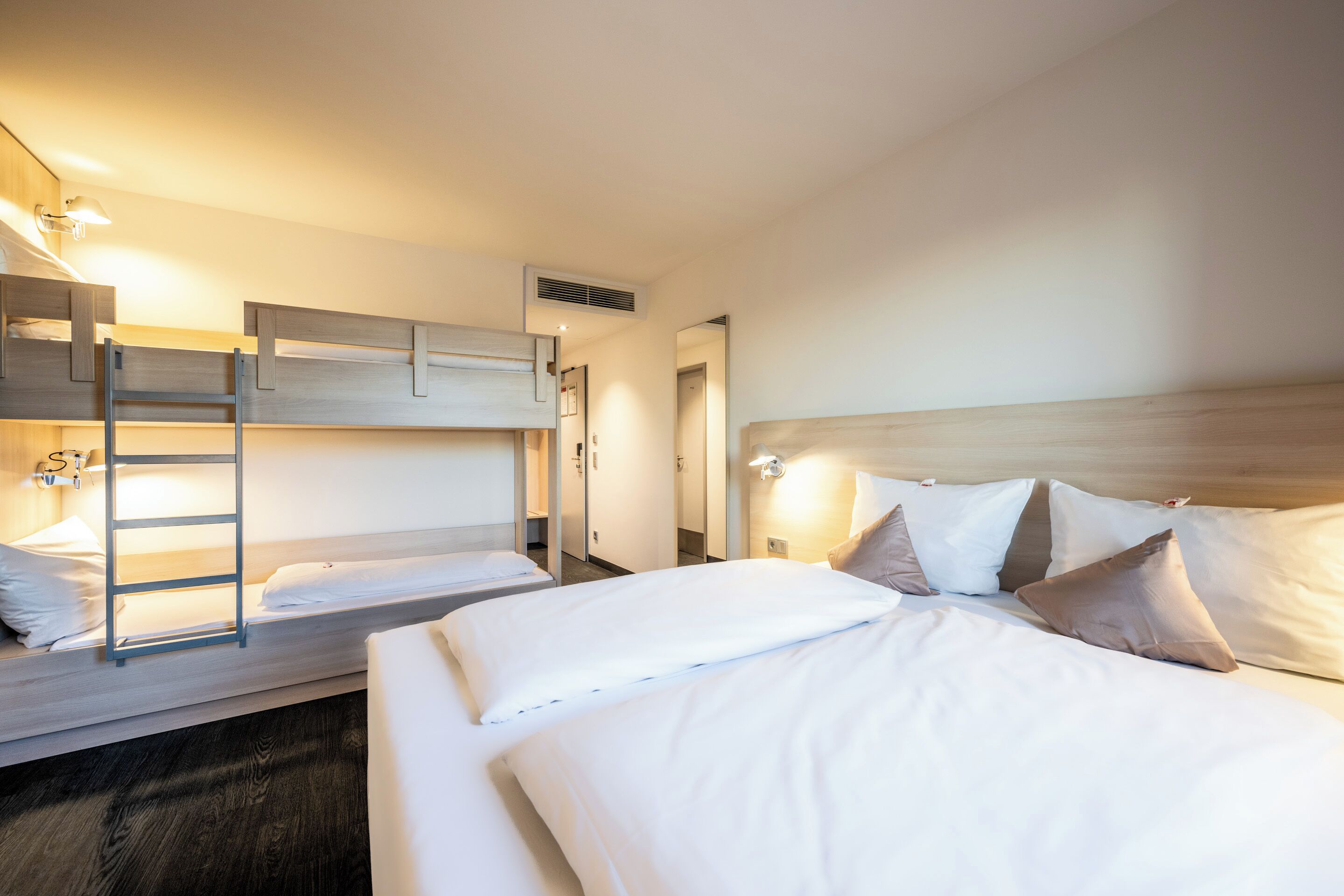 A hotel room with a bunk bed, a single bed, and a wooden headboard.