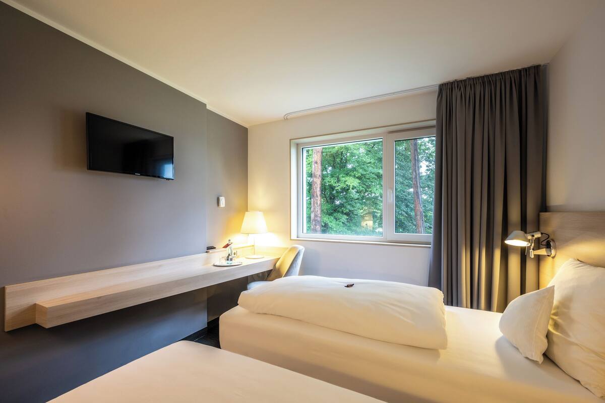 Hotellihuone, jossa on sänky, työpöytä, tuoli, seinälle asennettu televisio ja ikkuna, jossa on verhot.