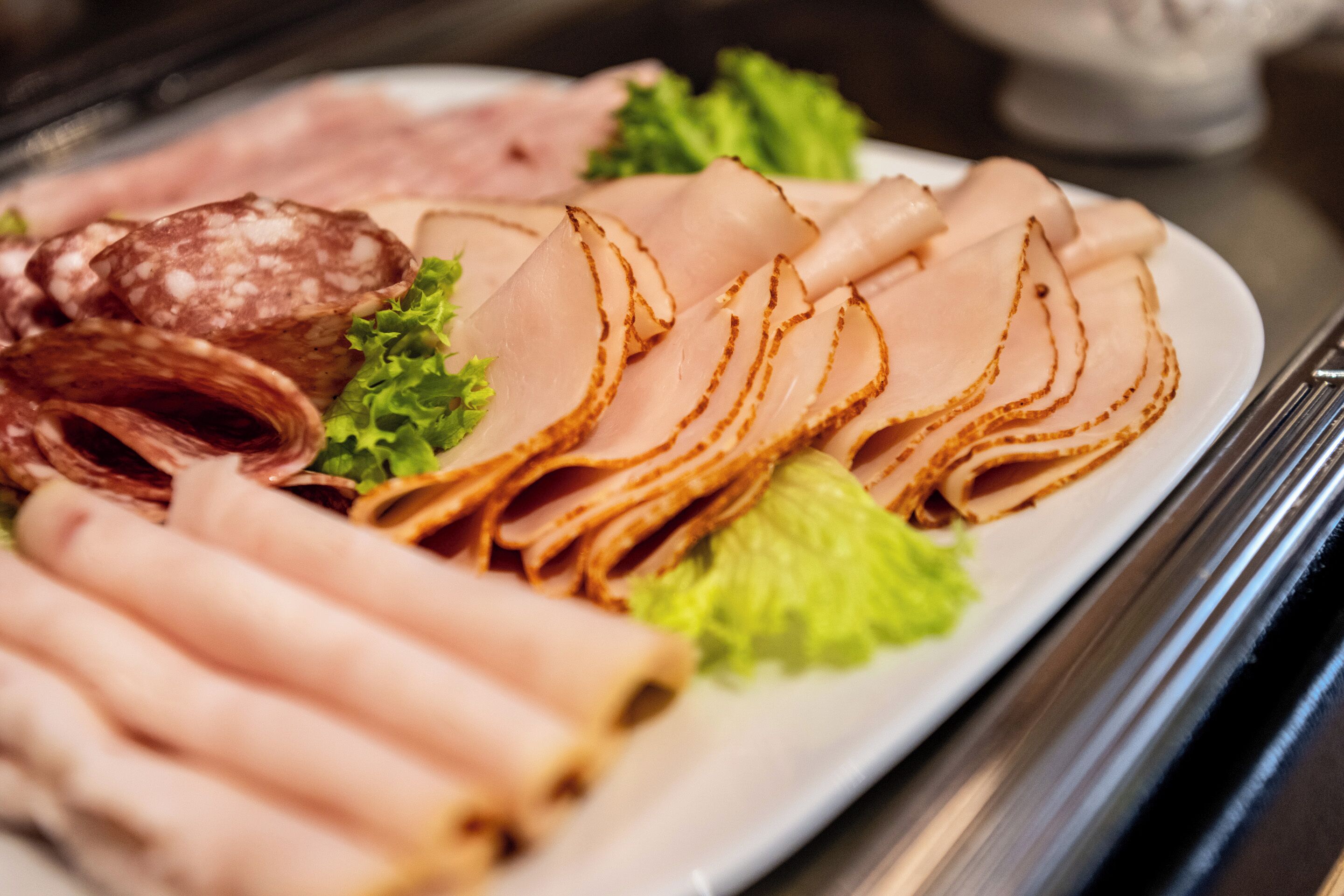 A plate of sliced meats including ham and salami, garnished with lettuce.