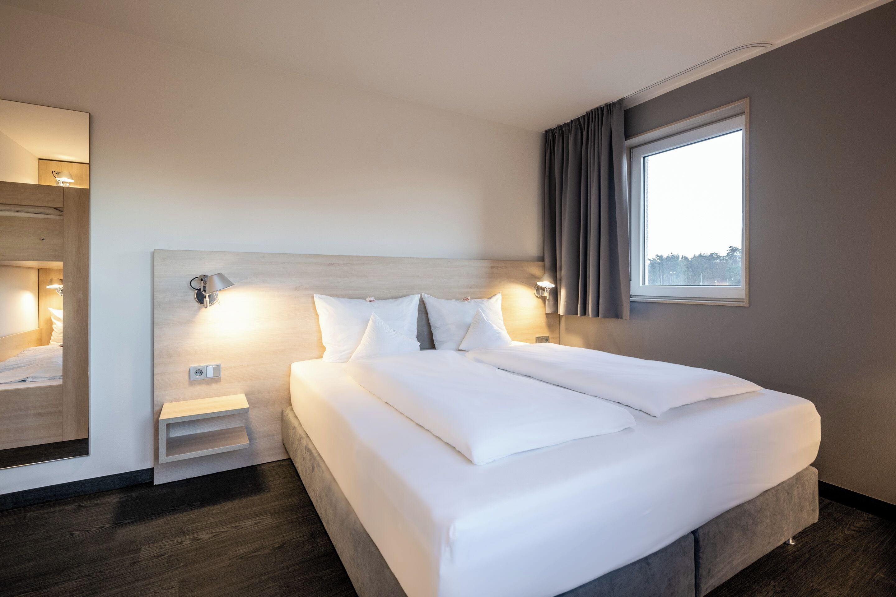 A modern hotel room with a large bed, bedside tables, and a window with curtains.