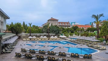 A poolside area with multiple lounge chairs and umbrellas, a large swimming pool, and surrounding greenery.