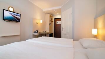 Une chambre d’hôtel comprenant un lit, un téléviseur fixé au mur, un bureau avec une chaise et une armoire.