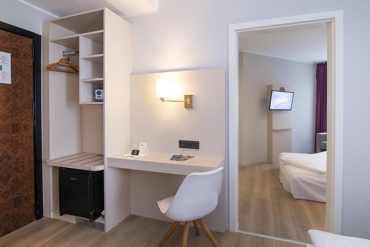 A compact hotel room with a desk, chair, bed, TV, and a walk-in closet.