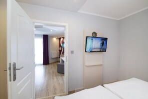 Habitación de hotel con cama, televisor montado en la pared, puerta de acceso a un baño y un pequeño rincón de descanso.