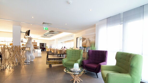 A modern hotel lobby with green and purple armchairs, a glass coffee table, and a white statue. - Nautic Hotel Bremerhaven (Bremerhaven)