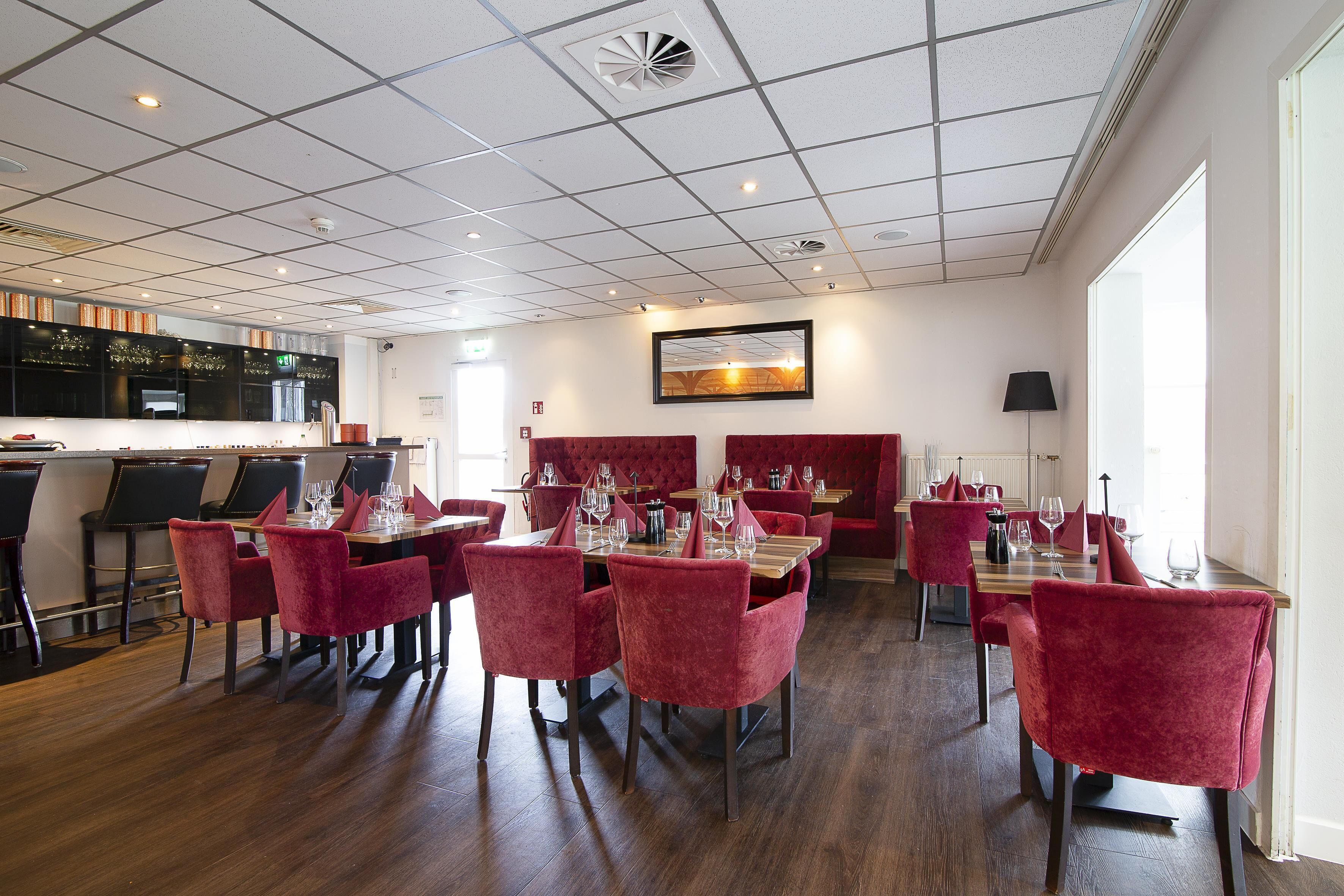 Een restaurant met rode bekleden stoelen, houten tafels en een betegeld plafond.