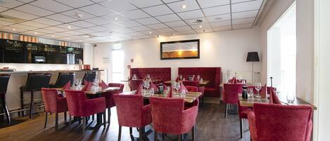 Een restaurant met rode bekleden stoelen, houten tafels en een betegeld plafond.