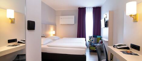 A hotel room with a bed, desk, chair, and a small table.