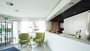 A modern reception area with a glass door entrance, two green armchairs, a small table, and a decorative vase. - Nautic Hotel Bremerhaven (Bremerhaven)
