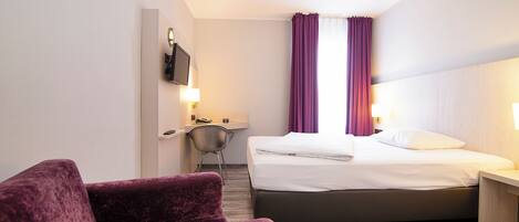 Habitación de hotel con una cama, un escritorio, una silla y un televisor montado en la pared.