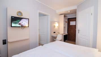 A hotel room with a bed, a desk, a chair, a TV mounted on the wall, and a door leading to a bathroom.