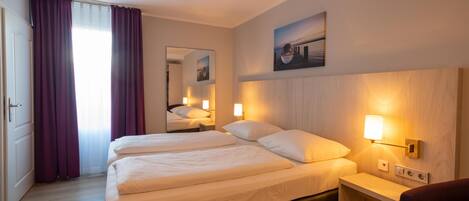 Een hotelkamer met twee bedden, een nachtkastje, een spiegel en een wandlamp.