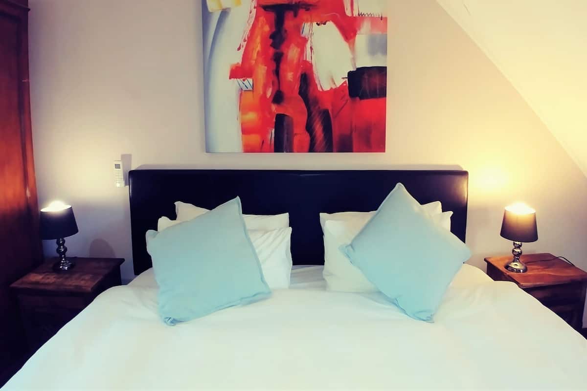 A hotel room with a large bed, two bedside tables, and a modern abstract painting on the wall.