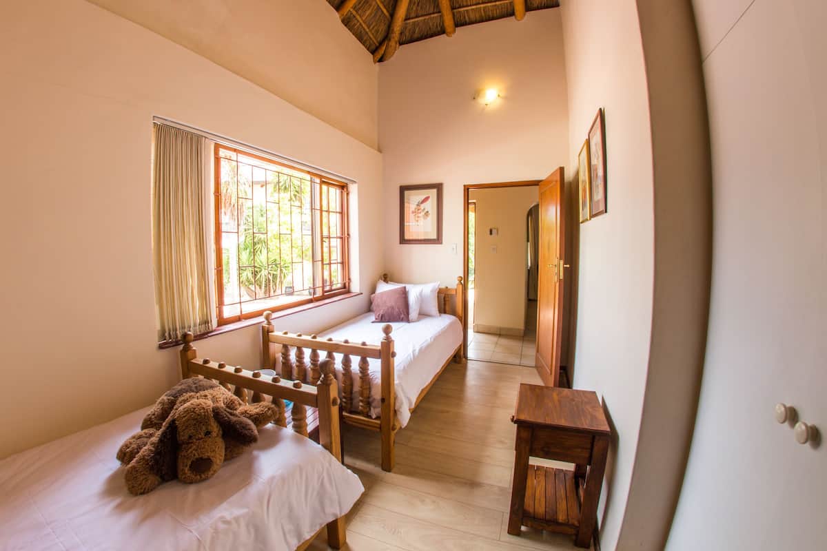 A bedroom with a wooden bed, a small table, a teddy bear, and a window with curtains.