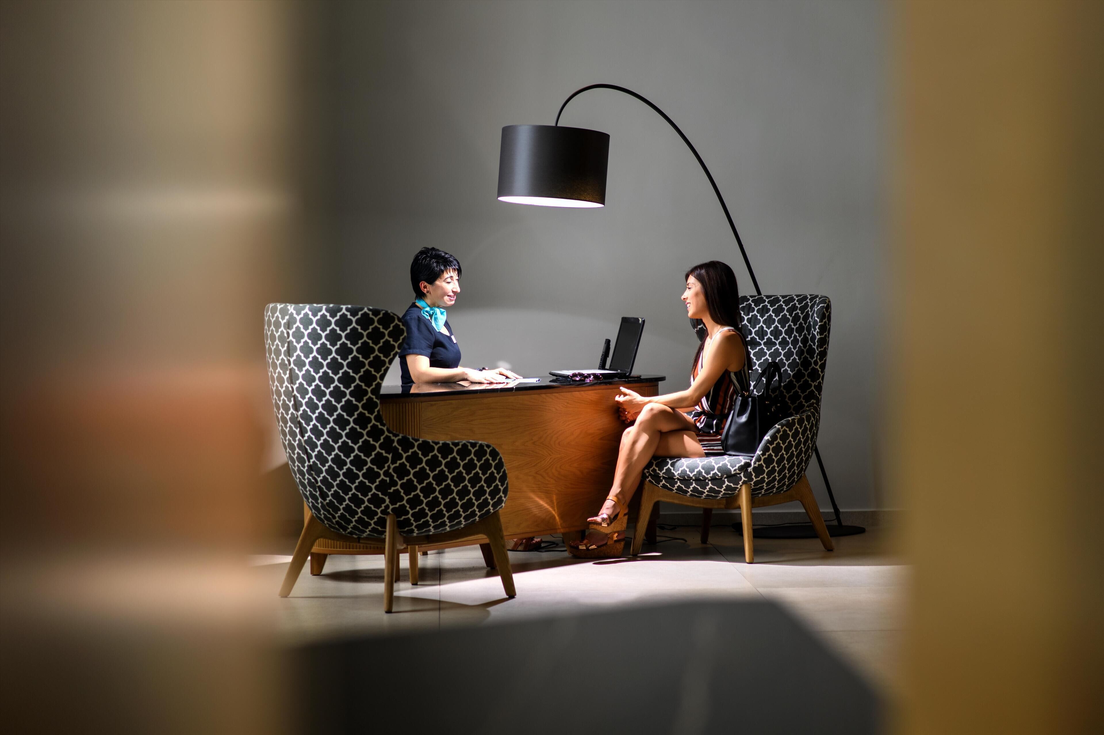 A modern office with two individuals seated at a desk, one using a laptop.