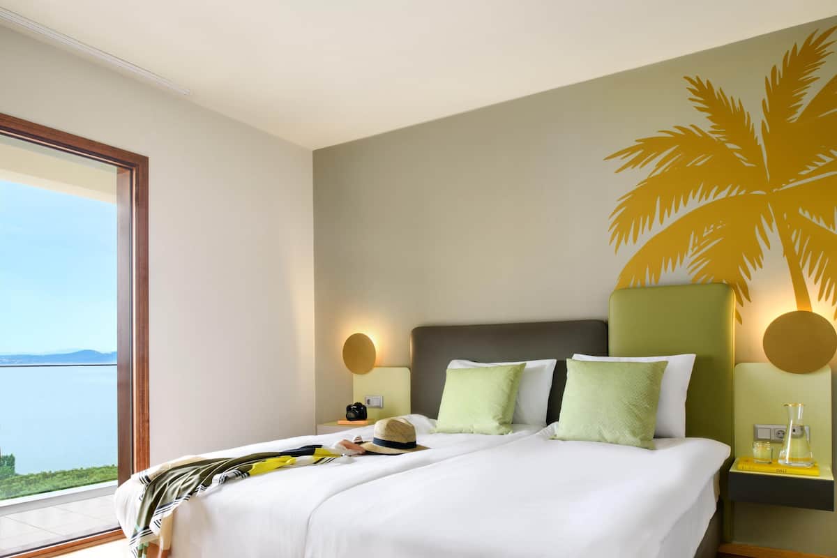 Ein Hotelzimmer mit einem großen Bett, Meerblick und einer Wandmalerei mit Palmen.