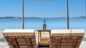 Um espaço de lounge à beira-mar, com cadeiras e mesa de madeira, uma garrafa de champanhe e um toldo.